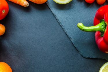 Vibrant assortment of fresh fruits and vegetables on a slate surface with ample copy space.