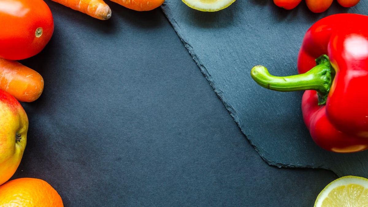 Vibrant assortment of fresh fruits and vegetables on a slate surface with ample copy space.