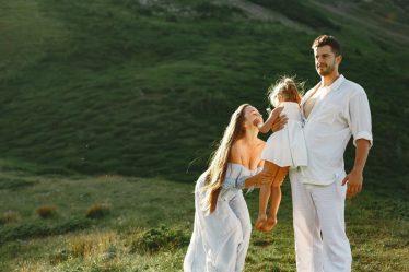 A joyful family of three in white clothing enjoying the outdoors on a sunny day.