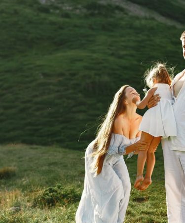 A joyful family of three in white clothing enjoying the outdoors on a sunny day.