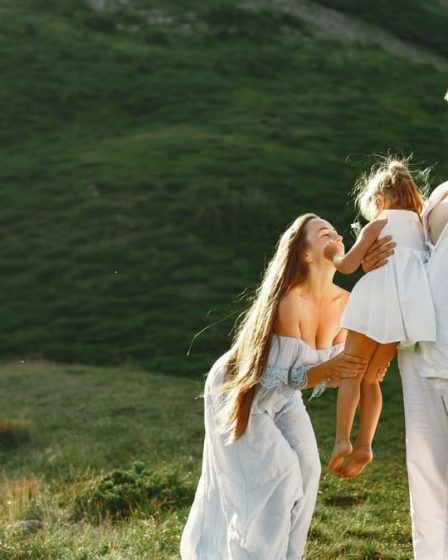 A joyful family of three in white clothing enjoying the outdoors on a sunny day.