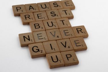 Wooden tiles spelling out 'Pause Rest But Never Give Up' on a white background.