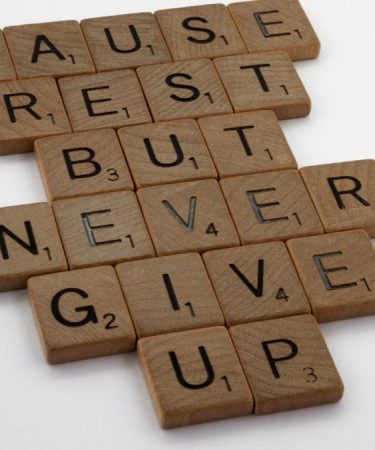 Wooden tiles spelling out 'Pause Rest But Never Give Up' on a white background.