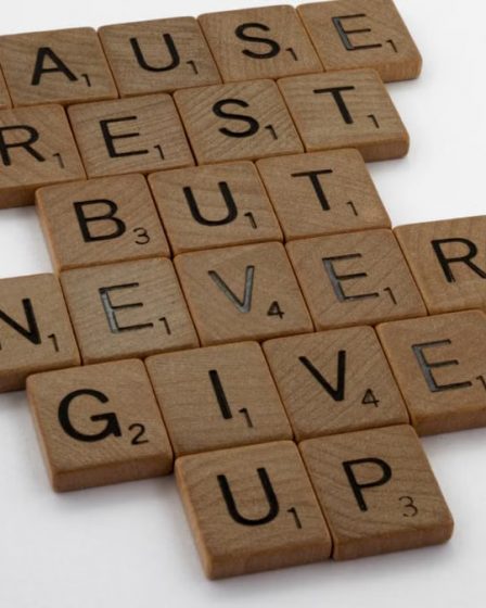 Wooden tiles spelling out 'Pause Rest But Never Give Up' on a white background.